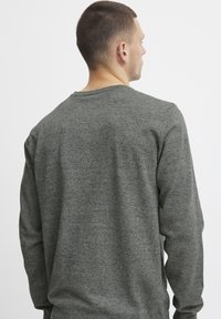 Suéter de color gris oscuro con mangas largas, cuello redondo y un acabado texturizado, que presenta un corte relajado y sin patrones ni herrajes visibles.