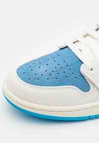 Gros plan d'une basket montrant un bout perforé bleu, une garniture en daim blanc cassé, des lacets blancs et une semelle en caoutchouc bleu texturé.
