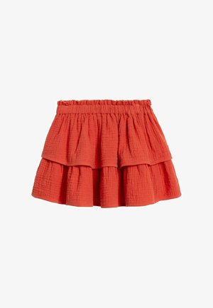 Jupe rouge à volants avec une taille élastique. Fabriquée en tissu texturé, elle comporte trois couches flottantes. Design décontracté, longueur mi-cuisse.