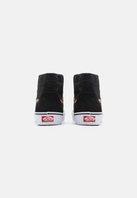 Černé semišové vysoké tenisky s prošívanou texturou, bílou gumovou podrážkou a červeným logem Vans na patě. Kovové akcenty zvýrazňují design.