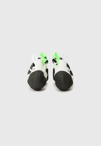 Black and white climbing shoes with rubber soles, featuring green and white heel straps and a streamlined, snug design.