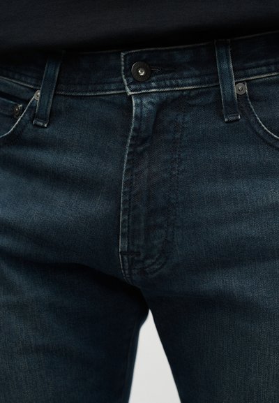 Σκούρο μπλε τζιν παντελόνι με εφαρμοστή σχεδίαση, πέντε τσέπες και εμφανείς ραφές. Το ύφασμα έχει ομαλή υφή και ελαφριά ξεθώριασμα.