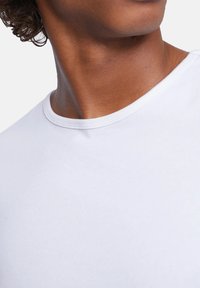 White cotton t-shirt featuring a round neck and smooth texture, with a snug fit at the collar and minimal design details.