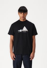 Sort bomulds t-shirt med et grafisk print af en hvid lastbil og et trekantet design med teksten "HUF" i midten. Enkel crew neck design.