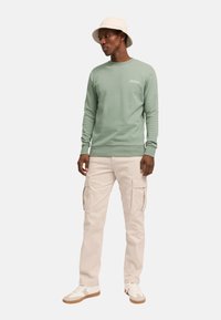 Sudadera verde menta con cuello redondo y puños acanalados, combinada con pantalones cargo beige que cuentan con múltiples bolsillos. Zapatillas blancas completan el look.