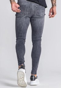 Jeans ajustados en denim gris oscuro con una textura suave. Presentan dos bolsillos traseros y un diseño ceñido, combinados con zapatillas blancas.