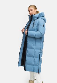 Svetlo modrý dlhý puffer kabát s kapucňou, s čiernou vnútornou podšívkou, zipsom na zapínanie a diagonálnymi postrannými zipsami, textúrovaný prešitý vzor.