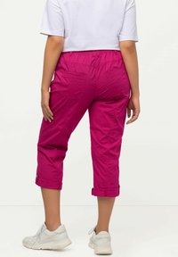 Pantalons courts fuchsia avec une taille élastique, deux poches arrière et des poignets retroussés. Associés à des chaussures de sport blanches.