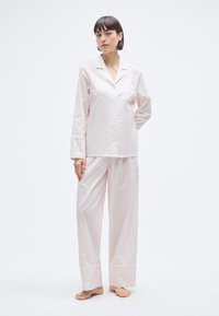 Ensemble de pyjama en coton rose clair composé d'une chemise à manches longues boutonnée, avec poche poitrine, et d'un pantalon droit à rayures fines.