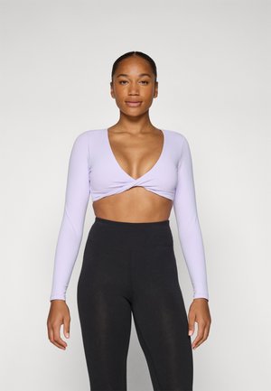 Crop top lilas à manches longues avec un profond décolleté en V et un design à l'avant tordu, associé à un legging noir taille haute. Texture de tissu lisse.