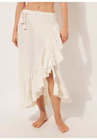Linned wrap nederdel i off-white med lagdelte volanger i kanten. Har en snøre i taljen med kvaster og en sideslids for bevægelsesfrihed.