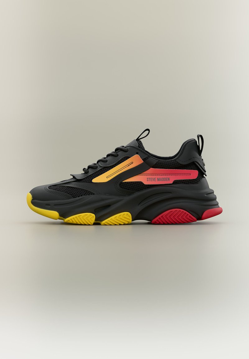 Fekete sportcipő sárga és piros talpak kiemelésekkel, narancssárga és piros oldalsávokkal, valamint „Steve Madden” felirattal az oldalsó panelen.