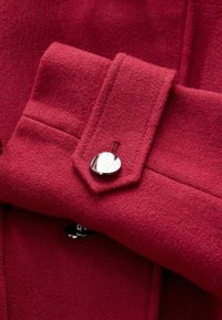 Red wool fabric features a structured collar with a shiny silver button detail. The texture is soft and slightly fuzzy, enhancing warmth.