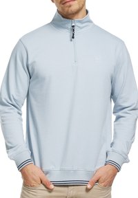 Sweat-shirt à fermeture éclair bleu clair avec poignets et ourlet côtelés, présentant un petit logo près du col. Fabriqué en tissu doux et texturé.