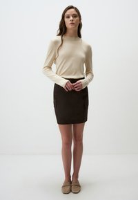 Beige lange mouw gebreide top met een ronde halslijn, gecombineerd met een donkerbruine mini rok met twee voorzakken. Tan instappers.