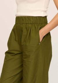 Pantalons taille haute vert olive en tissu léger, dotés d'une taille élastique et de poches latérales avec des détails en métal subtils.