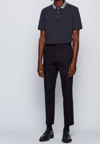 Polo triko s krátkými rukávy v tmavé barvě s bílým límcem, kombinované s elegantními černými kalhotami a černými společenskými botami. Hladký materiál, přiléhavý střih.