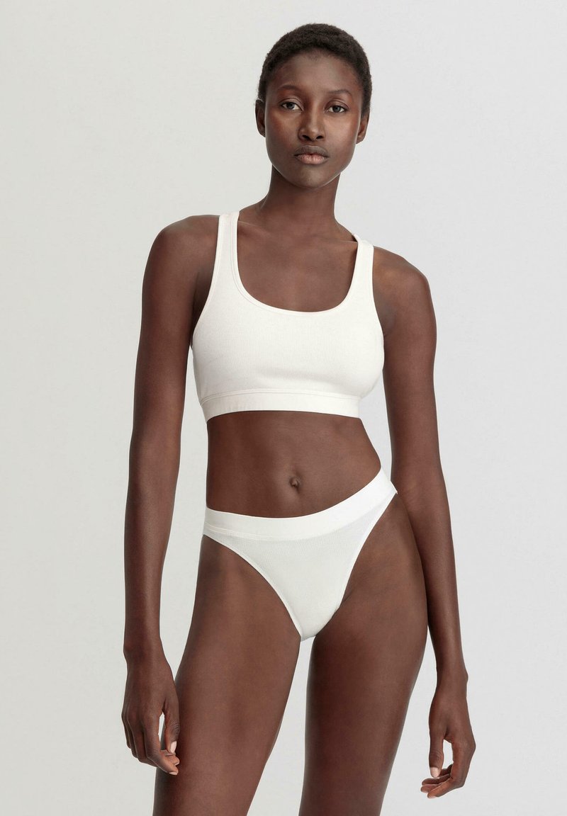 Weißes, geripptes Bralette und hochgeschnittenes Tanga-Set. Weicher, dehnbarer Stoff mit einer glatten Oberfläche und definierten Nähten. Minimalistisches Design, ohne Muster.