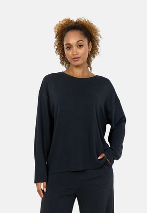 Long-sleeve black top with a loose fit, round neckline, and soft texture. Paired with matching dark pants, featuring side pockets.