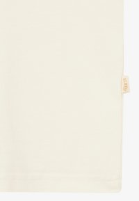 Cremfarbendes Baumwoll-T-Shirt mit glatter Textur, ausgestattet mit einem kleinen gewebten Etikett an der Seitennaht. Einfaches, schmuckloses Design.