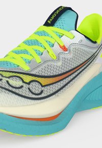 Αθλητικό παπούτσι με επάνω μέρος από ανοιχτό γκρι δίχτυ, νέον κίτρινα κορδόνια, μπλε γλώσσα και σόλα, πορτοκαλί και μαύρη λεπτομέρεια λογοτύπου στο πλάι.