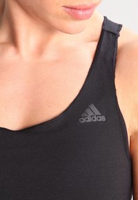 Top sportivo nero senza maniche con scollatura rotonda, realizzato in tessuto elasticizzato, con un logo Adidas grigio sobrio sul lato sinistro del petto.
