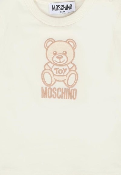 Maglietta infantile bianca con orso ricamato color sabbia e testo "Toy" con il logo "MOSCHINO" sottostante. Collo rotondo, tessuto morbido.