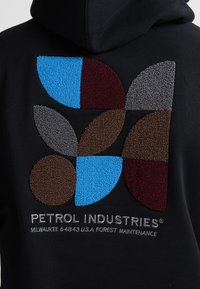 Mikina s kapucí v černé barvě s texturovaným barevným designem se tvary v modré, hnědé, šedé a burgundské. Logo značky pod designem.