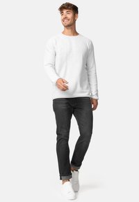 Suéter blanco de manga larga con cuello redondo, combinado con jeans oscuros y zapatillas blancas. La tela parece suave y lisa.