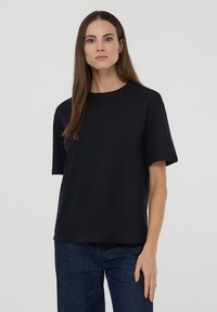 Czarny t-shirt z krótkim rękawem wykonany z bawełny, z okrągłym dekoltem i luźnym krojem, w połączeniu z ciemnoniebieskimi dżinsami.