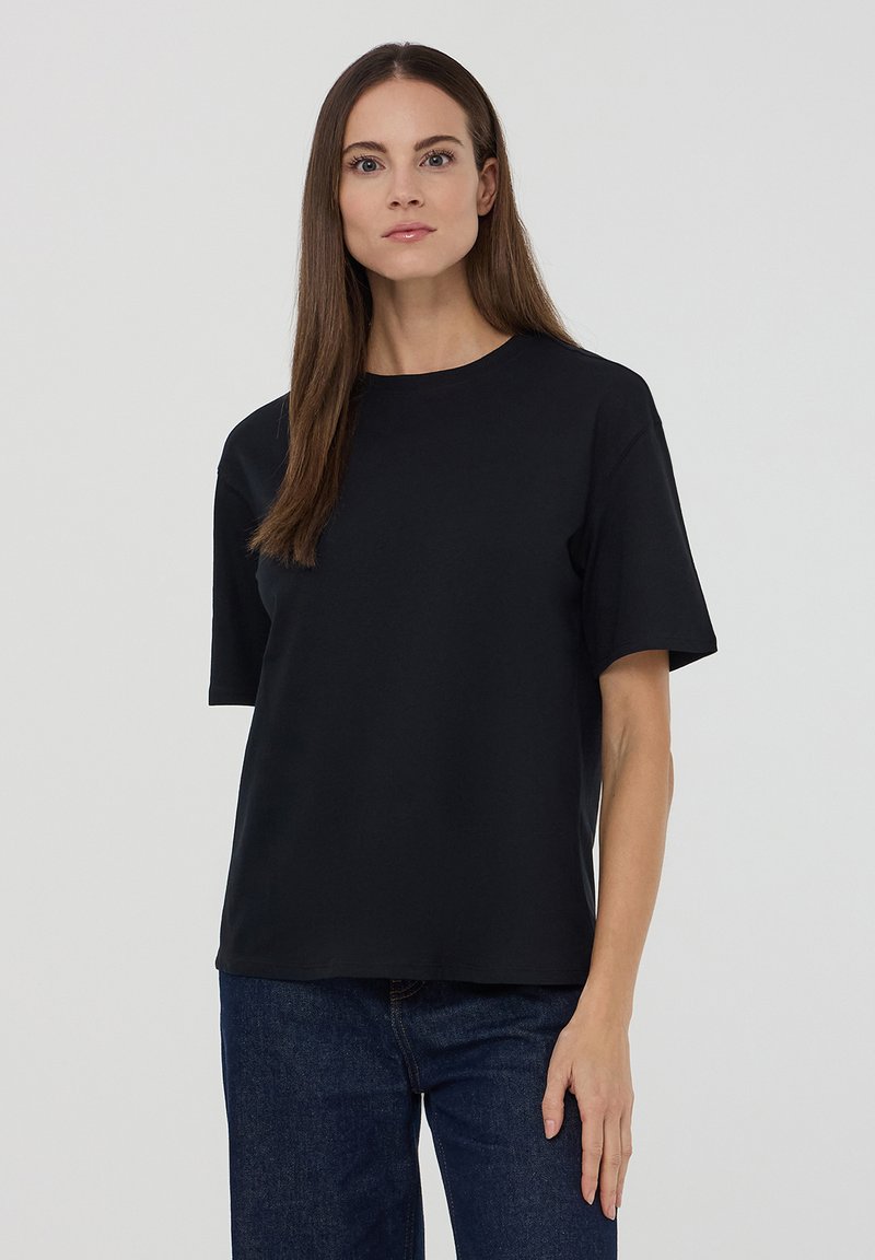 Czarny t-shirt z krótkim rękawem wykonany z bawełny, z okrągłym dekoltem i luźnym krojem, w połączeniu z ciemnoniebieskimi dżinsami.