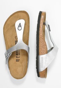 Sandále Birkenstock se stříbrným, texturovaným syntetickým svrchním materiálem, korkovou stélkou a černou gumovou podrážkou. Vyznačují se designem s přezkou a prstovým popruhem.