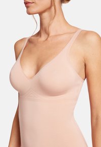 Body seamless rosa chiaro con scollatura a V, spalline sottili e coppe modellate. Texture liscia e design minimale con dettagli geometrici sottili.