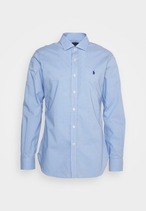 Chemise habillée à manches longues à carreaux bleu clair avec col boutonné et logo bleu marine brodé sur le côté gauche de la poitrine.