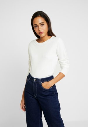 Witte, langwerpige gebreide trui met een ronde halslijn, gecombineerd met hoog getailleerde donkerblauwe denim jeans met zichtbare stiksels en zakken.
