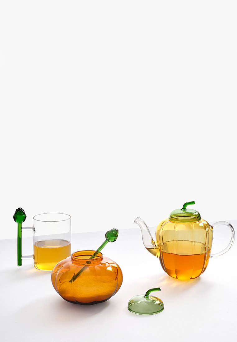 Pomarańczowy szklany czajnik z zieloną pokrywką i uchwytem, przezroczysta szklanka z zielonym akcentem oraz pomarańczowa miska z zieloną łyżką.