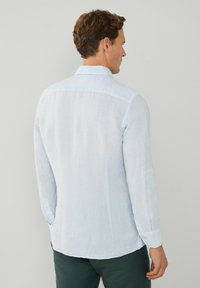 Camicia in lino azzurro chiaro con colletto a bottone, maniche lunghe e orlo curvo. Presenta una consistenza liscia e un lieve lucido.