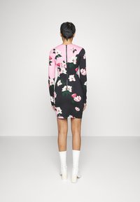 Robe à imprimé floral avec des sections noire et rose, manches longues, une fermeture éclair au dos et une silhouette ajustée. Portée avec des bottes blanches montantes.