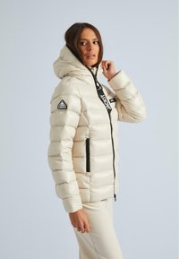 Hellbeige Daunenjacke mit Kapuze, Reißverschluss vorne und Taschen, ausgestattet mit einem dreieckigen Logopatch und schwarzen Reißverschlussakzenten.