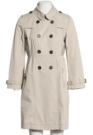 Trench-coat beige croisé avec fermeture par boutons, poignets ceinturés et poches latérales sur un mannequin blanc.