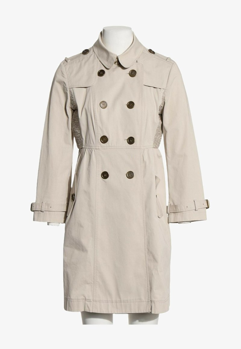 Trench-coat beige croisé avec fermeture par boutons, poignets ceinturés et poches latérales sur un mannequin blanc.