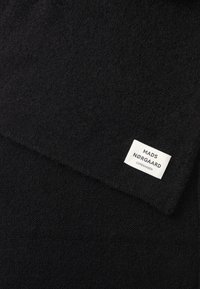 Sciarpa in lana nera con superficie texturizzata. Include un'etichetta bianca con la scritta "MADS NØRGAARD COPENHAGEN" stampata.
