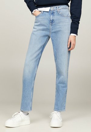Person wearing light blue straight-leg jeans, white sneakers, a navy sweatshirt, and a white shirt visible at wrists and waist.
