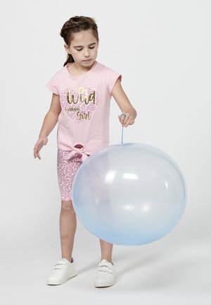 T-shirt rose avec un texte en or et imprimé léopard, associé à un short rose à imprimé léopard. L'enfant tient un grand ballon bleu semi-transparent.