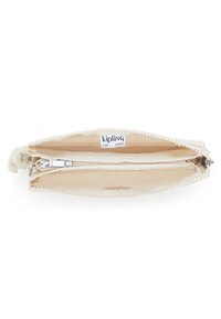 Crème-kleurige Kipling-pouch van zacht materiaal, met ritsluiting en contrasterende witte pomponafwerking. De binnenkant heeft een ritsvak en een logo-label.