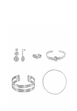 Fünf Schmuckstücke aus gehämmertem Silbermetall: Tropfenohrringe, zwei Manschettenarmbänder, ein Ring und eine dünne Creolen-Halskette vor weißem Hintergrund.