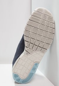 Marinblå sneakers med en strukturerad, mörk ovandel och en vit sula som har en ljusblå accent och ett multi-riktat greppmönster.