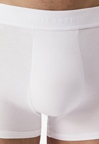 Boxers en coton blanc avec une texture douce et lisse, dotés d'une ceinture élastique de marque et d'un ajustement confortable autour des jambes et du siège.