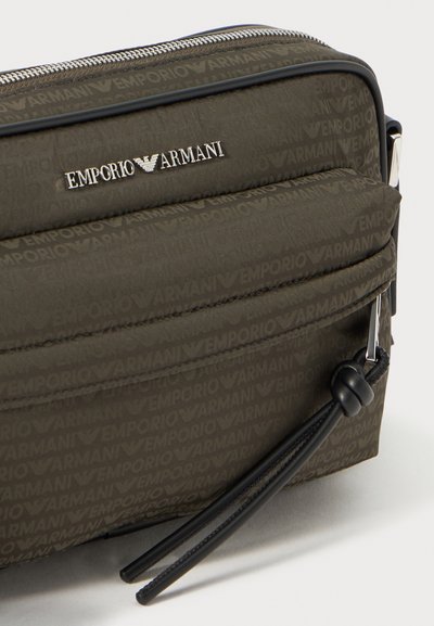 Geantă din țesătură tricotată, de culoare verde măsliniu, cu un model embossat "Emporio Armani". Dispune de un logo argintiu, închidere cu fermoar și accente negre.
