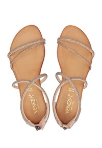Sandalen mit Riemen, die metallische Akzente, tanfarbene Ledersohlen und dünne glitzernde Riemen in neutralen Farben aufweisen. Markenlogo auf der Innensohle sichtbar.